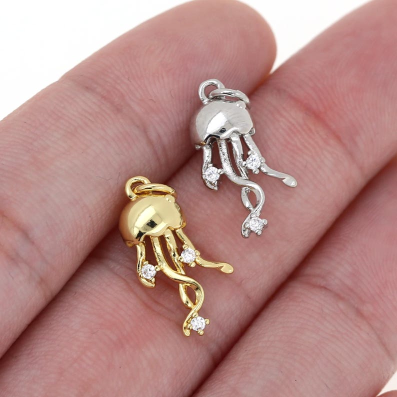 May include: Two silver and gold jellyfish charms with clear crystal accents. The charms are dangling from a loop and are perfect for jewelry making.