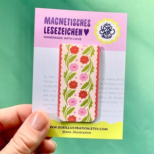 Könnte beinhalten: Ein rechteckiges magnetisches Lesezeichen mit cremefarbenem Hintergrund und einem wiederkehrenden Muster aus roten und rosa Blumen sowie grünen Blättern. Das Lesezeichen ist auf einer weißen Karte mit dem Text MAGNETISCHES LESEZEICHEN und SOEILLUSTRATION.ETSY.COM befestigt.