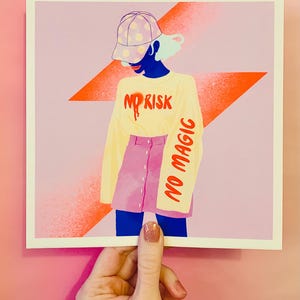 May include: A square art print featuring a stylized illustration of a figure wearing a polka-dot baseball cap, a long-sleeved cream shirt with the red text NO RISK, and a pink button-front skirt. The sleeve features the red text NO MAGIC.