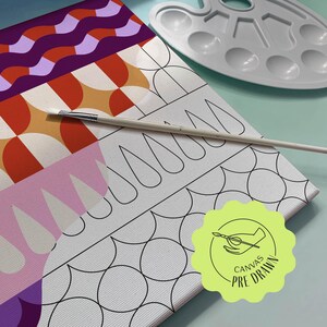Könnte beinhalten: Eine vorgemalte Leinwand mit einem geometrischen Design in Rot-, Orange-, Lila- und Rosatönen. Ein Pinsel liegt auf der Leinwand neben einer weißen Kunststoff-Farbpalette. Die Leinwand hat einen Aufkleber "Canvas Pre-Drawn".