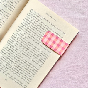 Könnte beinhalten: Ein rosa-weiß kariertes Lesezeichen steckt in einem Buch. Die Seiten des Buches sind sichtbar, mit deutschem Text und dem Titel "Geht hier alles zu Ende?" auf der Seite.