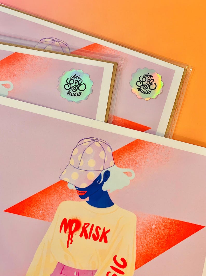 May include: A rectangular art print featuring a stylized illustration of a person wearing a polka-dot baseball cap and a cream-colored long-sleeve shirt with the red text NO RISK. The print includes a holographic sticker labeled Art Love Studio.