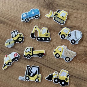 Könnte beinhalten: Eine Sammlung von zehn gestickten Aufnähern mit verschiedenen Baufahrzeugen, darunter ein blauer Wassertankwagen, gelbe Bagger, eine Straßenwalze, ein Betonmischer, ein Muldenkipper, ein Pritschenwagen, ein Gabelstapler und ein Nutzfahrzeug mit rotem Licht.