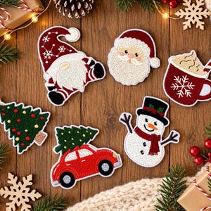 Puede incluir: Un conjunto de seis parches bordados con motivos navideños que incluye un gnomo con gorro rojo, una cara de Papá Noel, una taza de chocolate caliente con un bastón de caramelo, un árbol de Navidad verde, un coche rojo con un árbol y un muñeco de nieve.