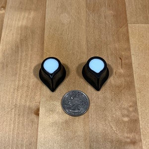 Könnte beinhalten: Zwei schwarze und weiße Gitarrenknöpfe mit einer spitzen Spitze. Die Knöpfe sind etwa so groß wie eine deutsche 20-Cent-Münze.