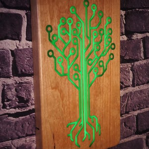 Puede incluir: Arte de pared rectangular de madera con un diseño de circuito verde en forma de árbol. La obra de arte está montada en una pared de ladrillo, mostrando el contraste entre la madera natural y la tecnología moderna.