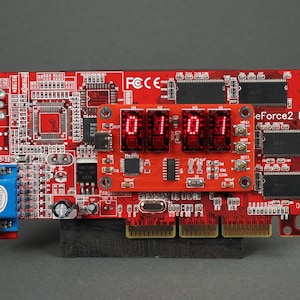 May include: A red circuit board with the text "eForce2 MX" and a digital display showing "0101". The board has various electronic components, including chips, connectors, and a blue VGA port. The display shows red digits.