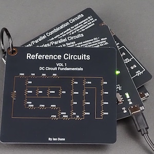 May include: A set of black reference circuit cards, held together by a metal ring. The cards display circuit diagrams and text, including "Reference Circuits VOL 1 DC Circuit Fundamentals" and "By Ian Dunn". A USB cable is connected to one card.