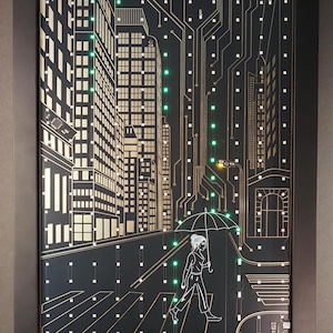 May include: A framed wall art piece featuring a black circuit board background with gold-colored line art of a city skyline and a person walking with an umbrella across a crosswalk. Small green LED lights are embedded throughout the design.