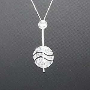 May include: A silver necklace with a textured round pendant and a smaller textured round charm hanging from it.