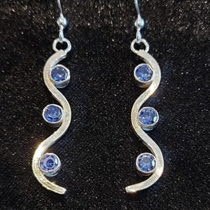 May include: Silver earrings with a wavy design and three blue gemstones.
