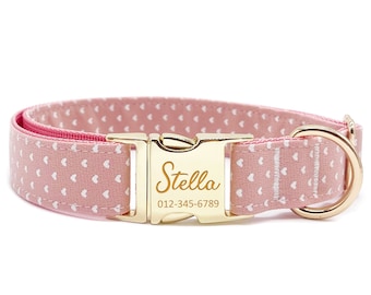 May include: Pink dog collar with white heart pattern and gold buckle. The buckle has the name "Stella" and phone number "012-345-6789" engraved on it.