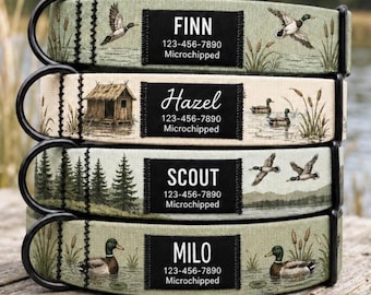 May include: Four pet collars with black metal D-rings, featuring nature-themed prints of ducks, cattails, cabins, and pine trees. Each collar has a black rectangular patch with white text displaying names, phone numbers, and the word Microchipped.