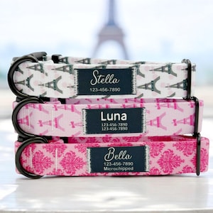 May include: Three pink and white dog collars with black buckles and personalized name tags. The collars feature a pattern of the Eiffel Tower and the name tags include the dog's name, phone number, and "Microchipped".