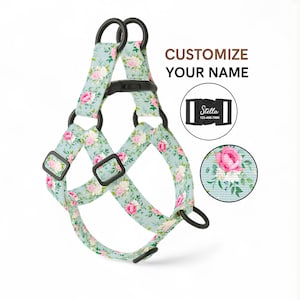 May include: A dog harness featuring a floral design of pink roses and green foliage on a pale blue backdrop. The harness has black fittings and the text "CUSTOMIZE YOUR NAME". A close-up shows a buckle with the name "Stella" and a phone number.