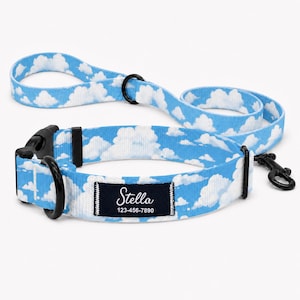 May include: A light blue dog collar and matching leash set featuring a white cloud pattern. The collar includes a black plastic buckle, a black metal D-ring, and a rectangular black fabric tag with the white text Stella and 123-456-7890.