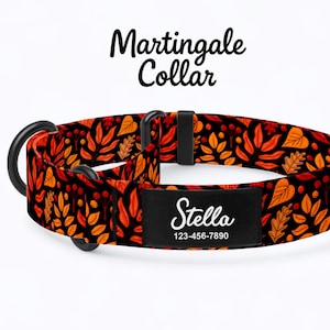 May include: Martingale dog collar with a black background and a pattern of orange and yellow leaves. The collar has a black metal ring and a black name tag that says "Stella" and a phone number.