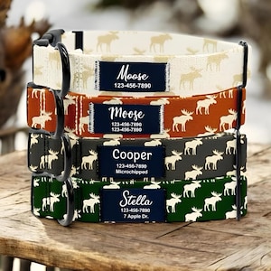 May include: Four dog collars stacked on a wooden surface. Each collar has a different colour and pattern featuring moose silhouettes. The collars have black metal hardware and a navy blue name tag with white text. The names "Moose", "Cooper", and "Stella" are visible.