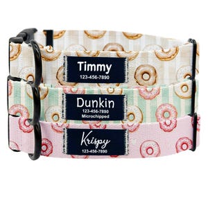 May include: Three dog collars with black buckles and name tags. The collars feature a repeating pattern of donuts on different colored backgrounds: beige, mint green, and pink. Each tag displays a name and phone number.