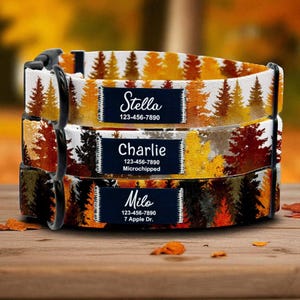 May include: Three personalised dog collars stacked on a wooden surface. Each collar features a forest pattern in shades of orange, yellow, and brown. Each collar has a navy blue name tag with a name and phone number. The names are Stella, Charlie, and Milo.
