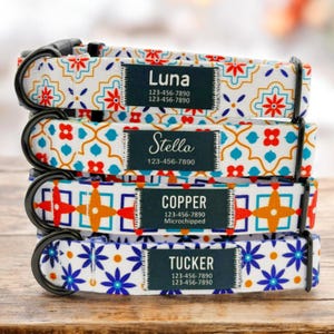 Puede incluir: Cuatro collares de perro coloridos con etiquetas de nombre personalizadas. Los collares presentan un fondo blanco con un patrón geométrico en tonos de azul, naranja y rojo. Las etiquetas de nombre son negras con texto blanco e incluyen el nombre del perro, el número de teléfono y "Microchipeado" para un collar.