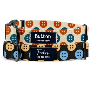 May include: Two dog collars with button patterns. One collar is cream with orange and blue buttons, the other is black with yellow and blue buttons. Each collar has a navy blue name tag with a name and phone number.