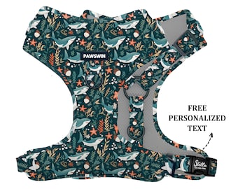 May include: A blue and green dog harness with a shark and seaweed pattern. The harness has a mesh lining and adjustable straps. The text "PAWSWIN" is printed on the harness. The harness has a buckle for attaching a leash. The text "FREE PERSONALIZED TEXT" is printed on the image.