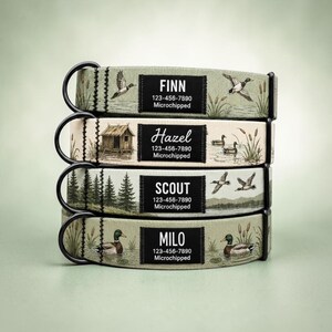 May include: A stack of four pet collars featuring nature-themed prints of ducks, cabins, and pine trees. Each collar has a black metal D-ring and a rectangular black patch with white text displaying names like Finn, Hazel, Scout, and Milo.