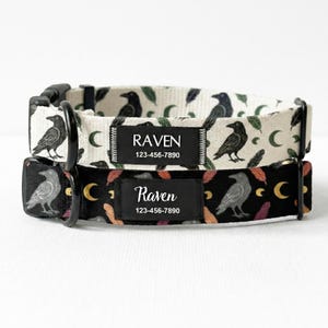 May include: Two dog collars with black hardware. One collar is cream-colored with black raven and leaf patterns. The other is black with raven, feather, and crescent moon patterns. Each collar has a black label with the name "Raven" and a phone number.