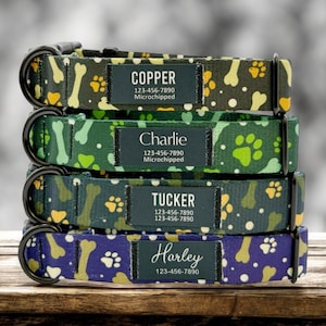 May include: Four dog collars stacked on top of each other. The collars are green, blue, and black with a bone and paw print pattern. Each collar has a black tag with white text that says the dog's name, phone number, and "Microchipped". The names on the tags are Copper, Charlie, Tucker, and Harley.