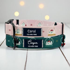 May include: Two personalized dog collars. One is pink with a repeating pattern of snow globes and houses, the other is dark green with a similar design. Each collar has a name and phone number printed on a navy blue label.