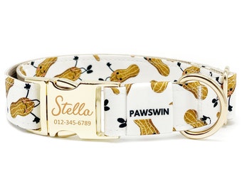Puede incluir: Collar blanco para perros con un estampado repetido de cacahuetes sonrientes. El collar tiene una hebilla y una anilla en D de metal dorado. El nombre "Stella" y un número de teléfono están grabados en la hebilla. La marca "PAWSWIN" está impresa.