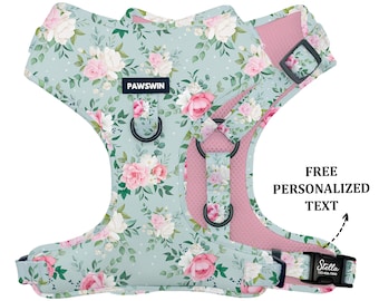 May include: A light blue dog harness with a floral pattern featuring pink roses and green leaves. The harness has a pink mesh lining and a black adjustable strap with the text "PAWSWIN" on it. The harness also has a black adjustable strap with a blue buckle that says "Stella" on it. The text "FREE PERSONALIZED TEXT" is written in white on a black background with an arrow pointing to the buckle.