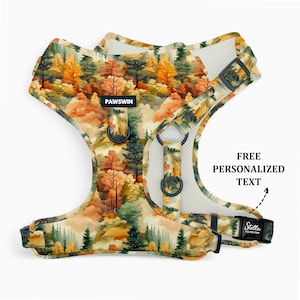May include: Dog harness with a colorful forest scene print. The harness features a watercolor design with trees in shades of orange, green, and yellow. Includes the text "PAWSWIN" and "Stella" with a phone number. The harness has adjustable straps and metal D-rings.