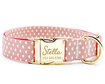 May include: Pink dog collar with white heart pattern and gold buckle. The buckle is engraved with the name "Stella" and a phone number.