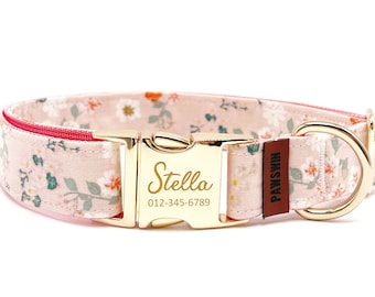 Puede incluir: Un collar floral para perros con hebilla y herrajes dorados. El collar es de color rosa claro con un estampado de flores blancas y naranjas y hojas verdes. El nombre "Stella" y un número de teléfono están grabados en la hebilla.