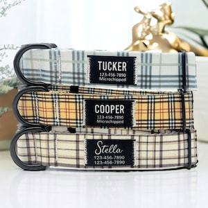 May include: Three dog collars with plaid patterns in blue, yellow, and brown. Each collar has a black tag with a name, phone number, and the words "Microchipped". The names on the tags are Tucker, Cooper, and Stella.