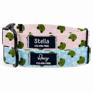 May include: Two personalized dog collars. One is light pink with a frog and flower pattern, the other is light blue with the same pattern. Each collar has a black buckle and a name tag that reads "Stella" and "Roxy" with a phone number.