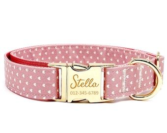 May include: Pink dog collar with white heart pattern and gold buckle. The buckle has the name "Stella" and phone number "012-345-6789" engraved on it.