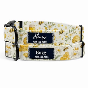 May include: Two dog collars with a bee-themed pattern. The cream-coloured collars display yellow bees, honeycombs, and flowers. Each collar has a navy blue tag with a name and phone number: "Honey" and "Buzz".