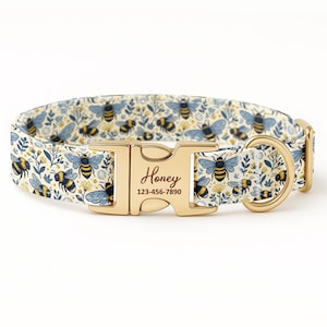 May include: A dog collar with a bee and floral pattern in cream, blue, and yellow. The gold-colored buckle has the name "Honey" and a phone number. The collar is designed for pets.