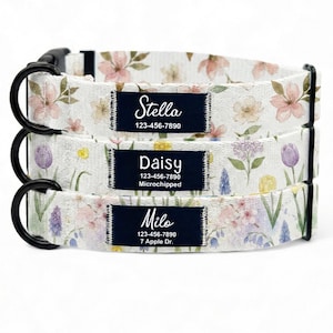 Puede incluir: Tres collares florales para perros con herrajes negros. Cada collar tiene una etiqueta azul marino con el nombre y la información de contacto de la mascota. Los collares presentan un fondo blanco con flores rosas, moradas y amarillas.