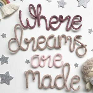 May include: A nursery wall decor set with the words "Where dreams are made" in pink and brown yarn. The words are surrounded by silver glitter stars.