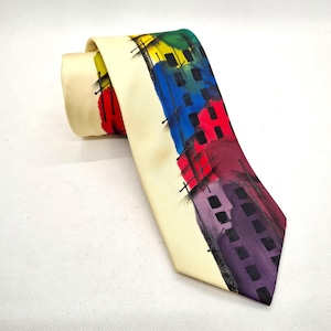 May include: A cream-coloured silk tie with a colourful abstract design of buildings. The buildings are painted in shades of red, blue, yellow, green, and purple.