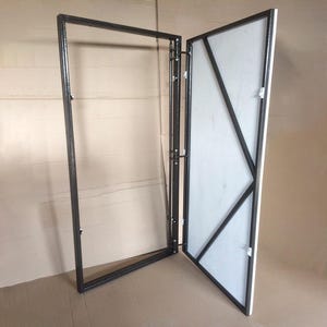 May include: A black metal frame with a white panel, featuring a geometric design. The frame is hinged, suggesting a door or screen. The panel has black diagonal supports. The item is set against a neutral background.
