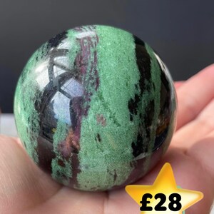 May include: Green, black and purple gemstone sphere. The sphere is polished and has a smooth surface.