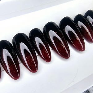 May include: Set of ten long, almond-shaped false nails with a black to red ombre glitter finish.