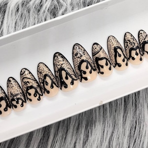 May include: Set of ten false nails with a nude base and black lace design. The nails are shaped like almond and have a dripping effect.