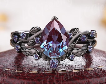 May include: A pear-shaped, iridescent gemstone ring set in black gold with a delicate leaf design and smaller gemstones. The ring is in a red velvet ring box.