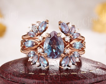 May include: A pear-shaped alexandrite gemstone ring set in rose gold with a halo of smaller alexandrite and diamond stones. The ring is designed with a split band, creating a unique and elegant look.
